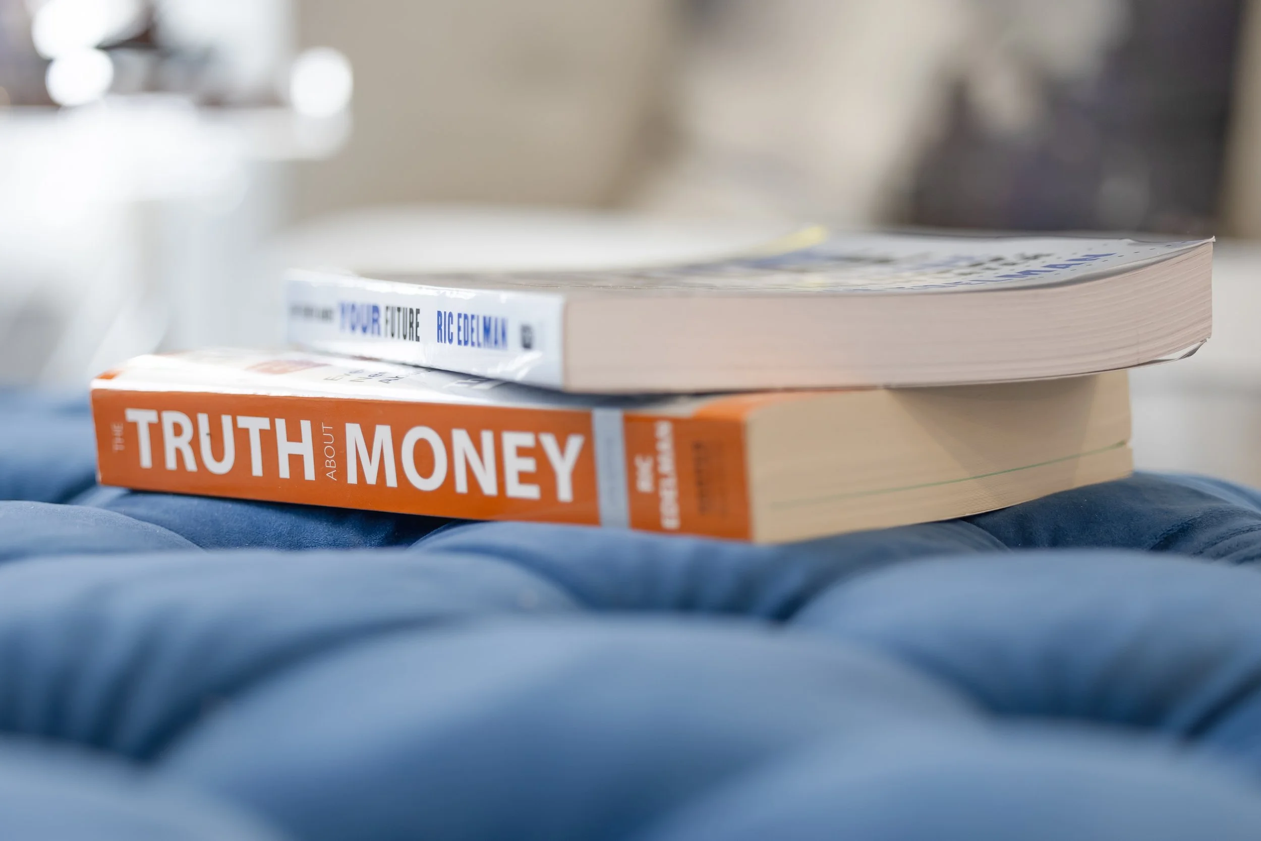 Stack of financial planning books, including “The Truth About Money,” resting on a blue upholstered bench.