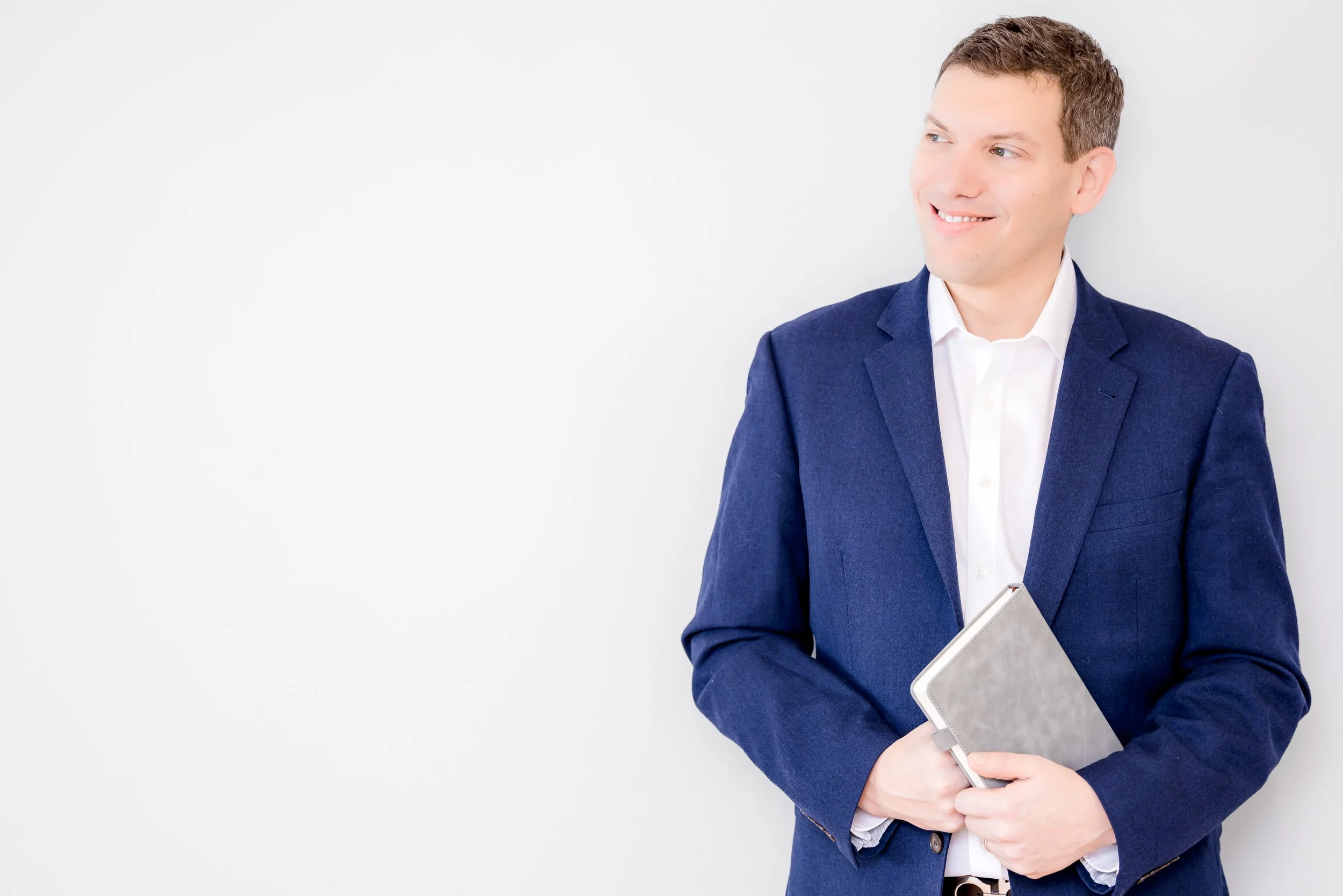 Josh Joffe holding a notebook and smiling, wearing a navy blazer and white shirt against a light background.