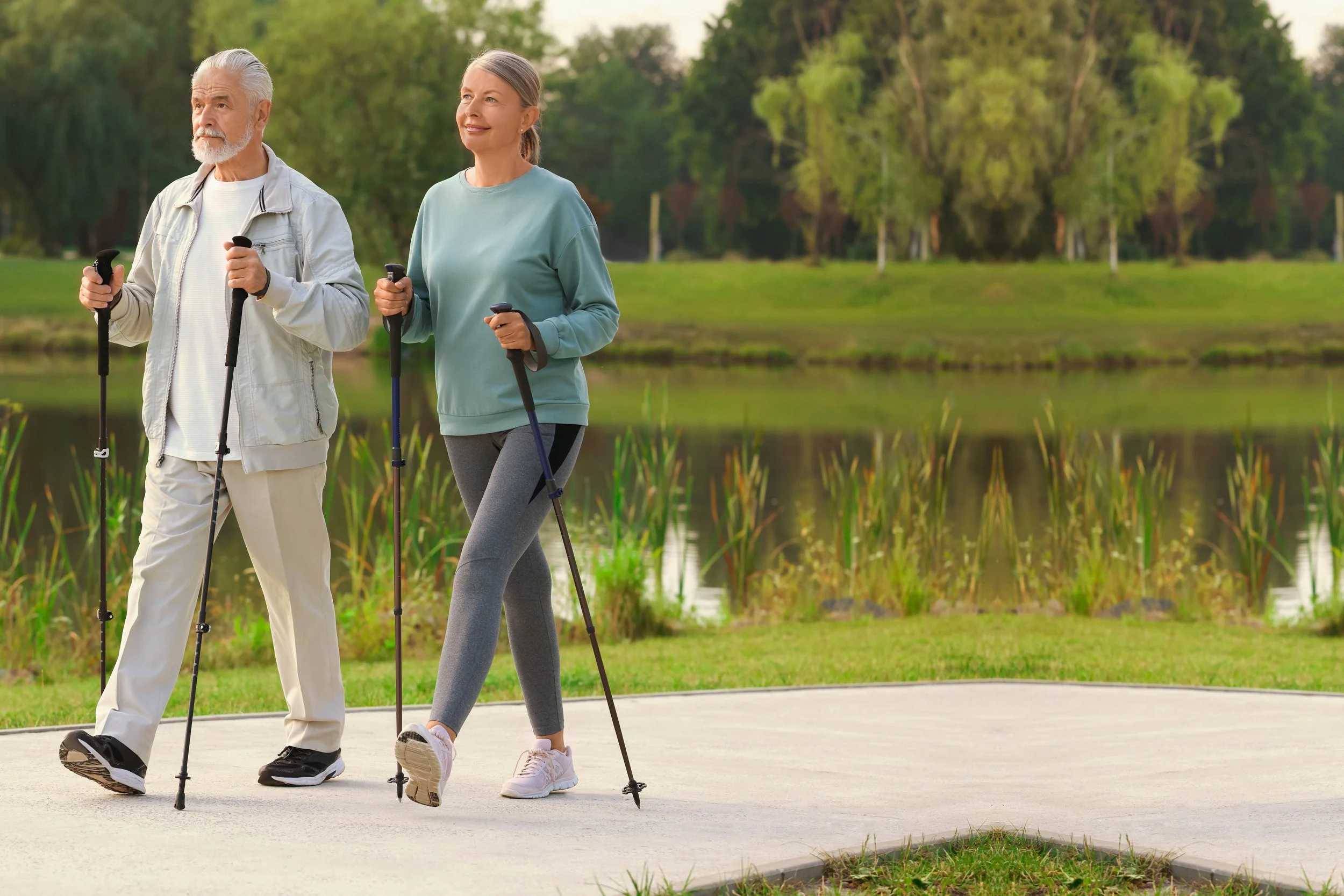 An elderly man and woman walking with canes near a pond in a park.