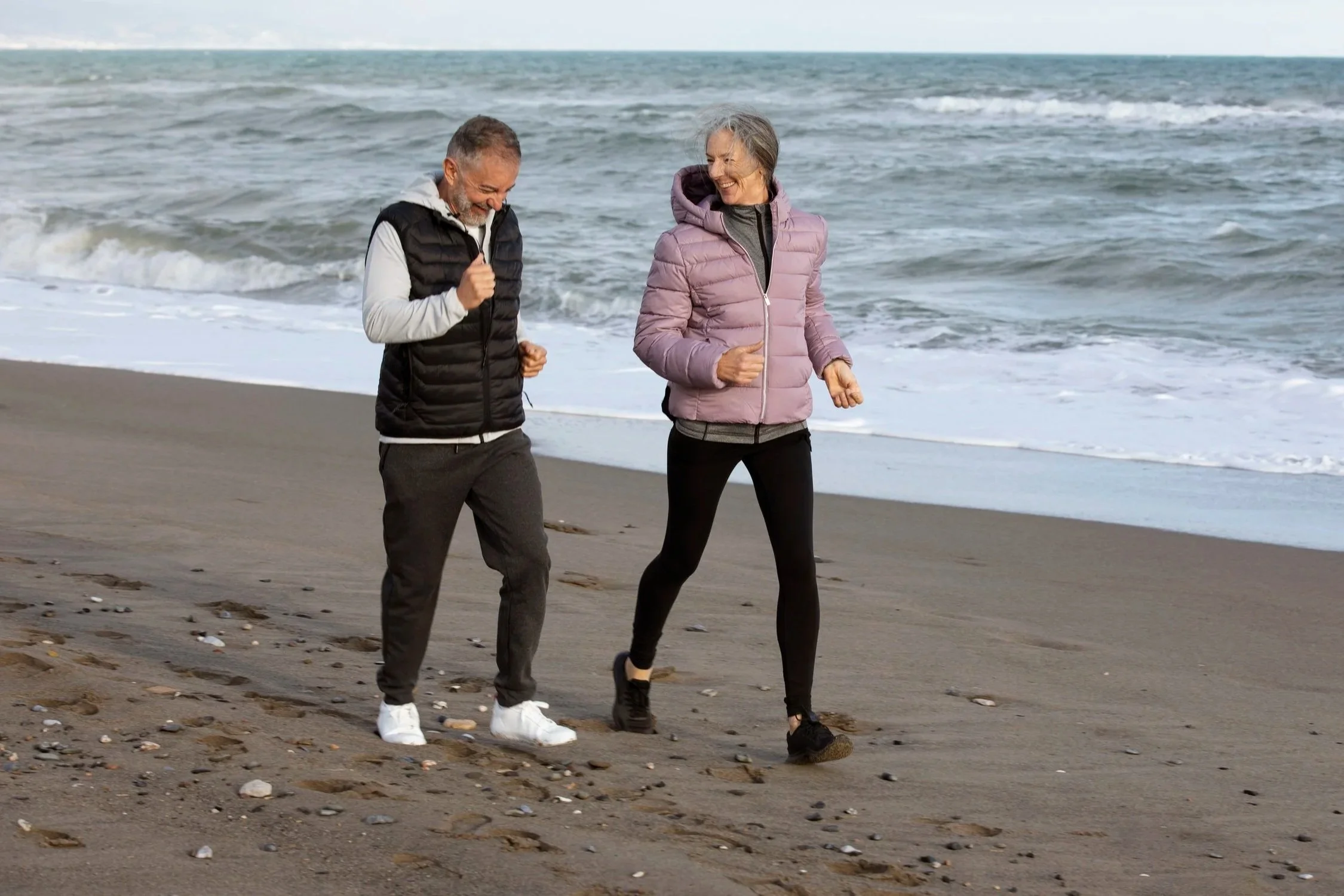 A man and a woman walking along the beach, smiling and enjoying each other's company.
