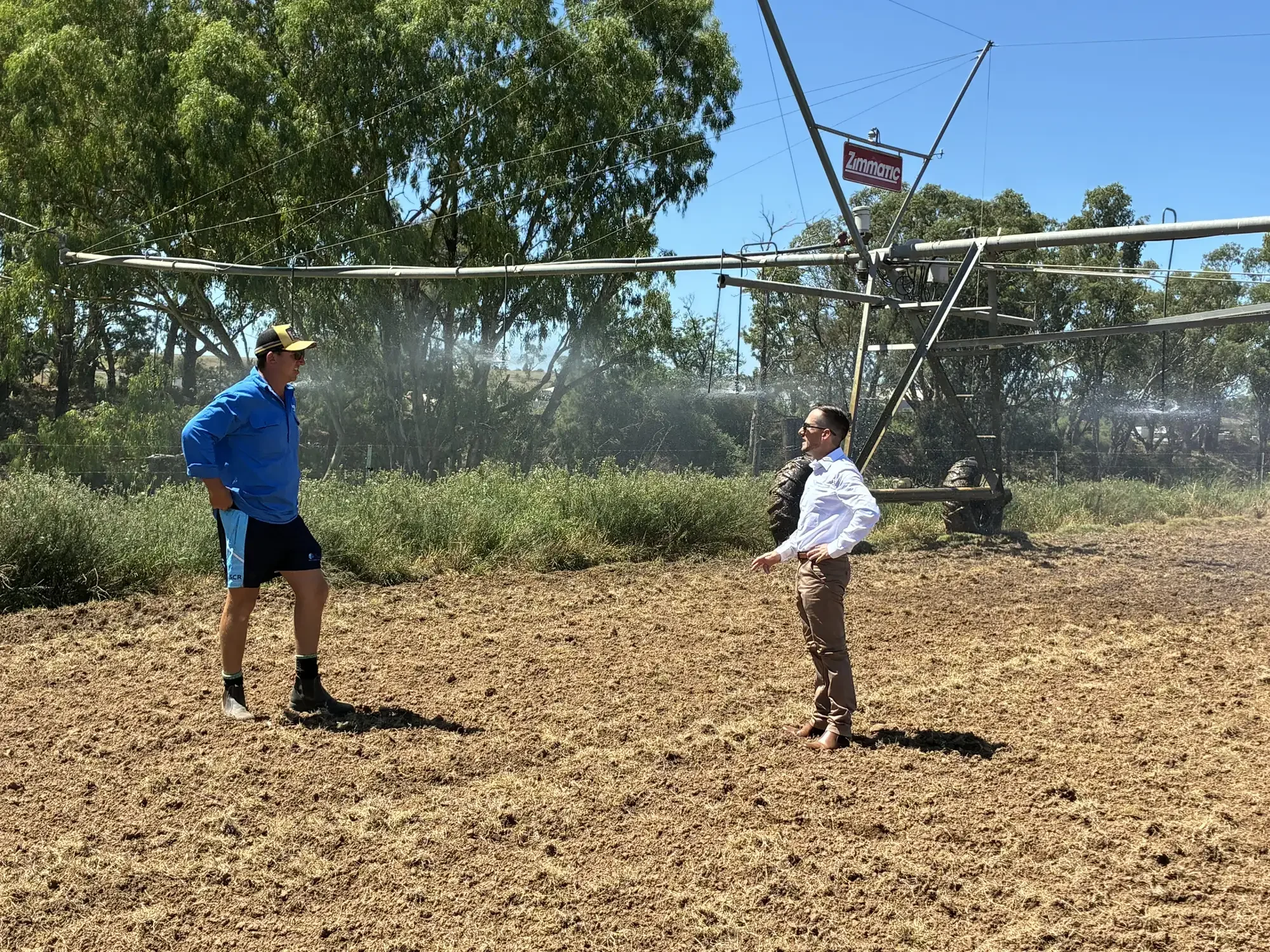 rob and a client standing in a paddock, discussing water law and nrar dealings. In the background there is a pivot, grasses and large trees