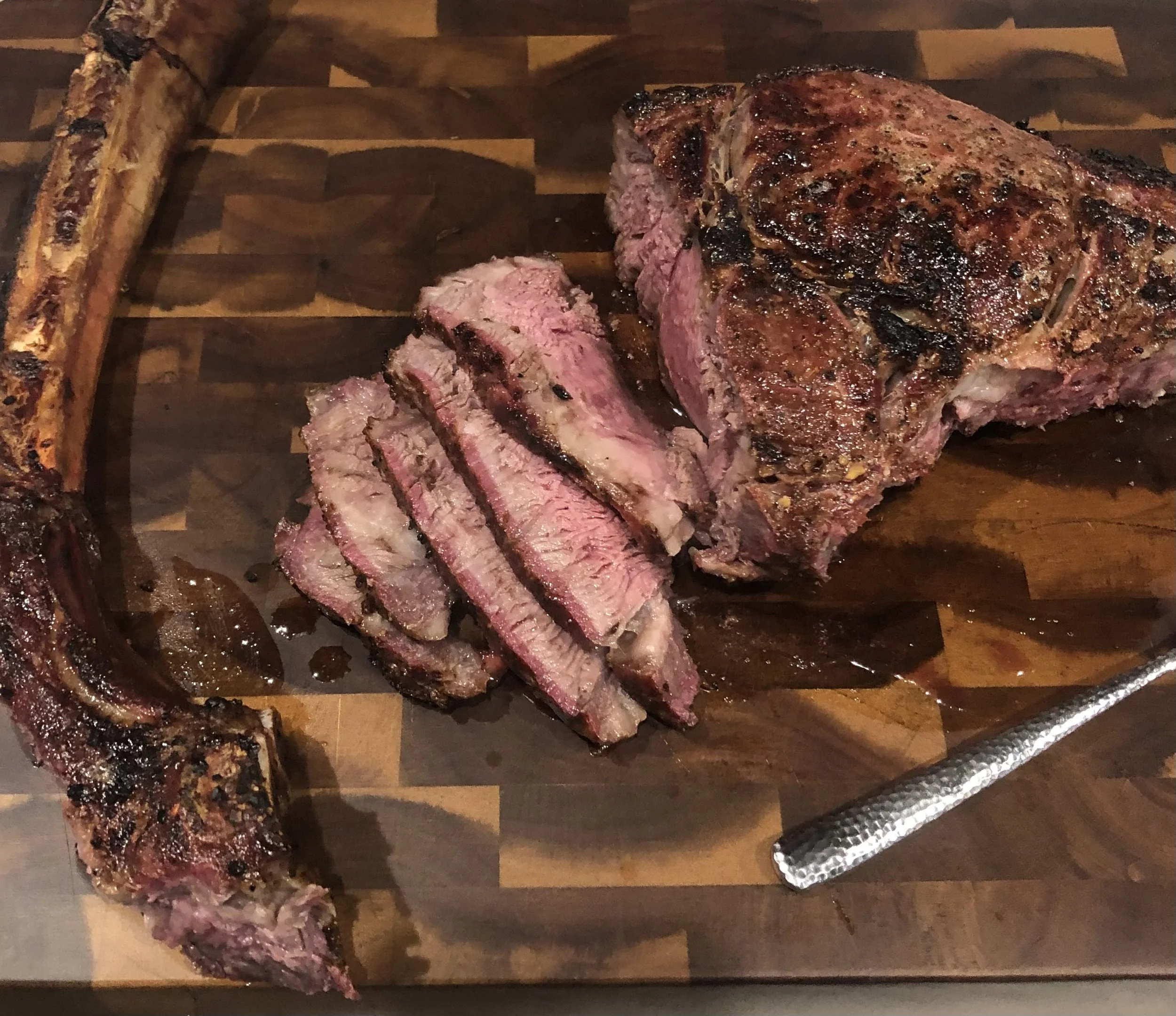 Slices of cooked beef steak on a wooden cutting board with a piece of grilled beef rib on the side.