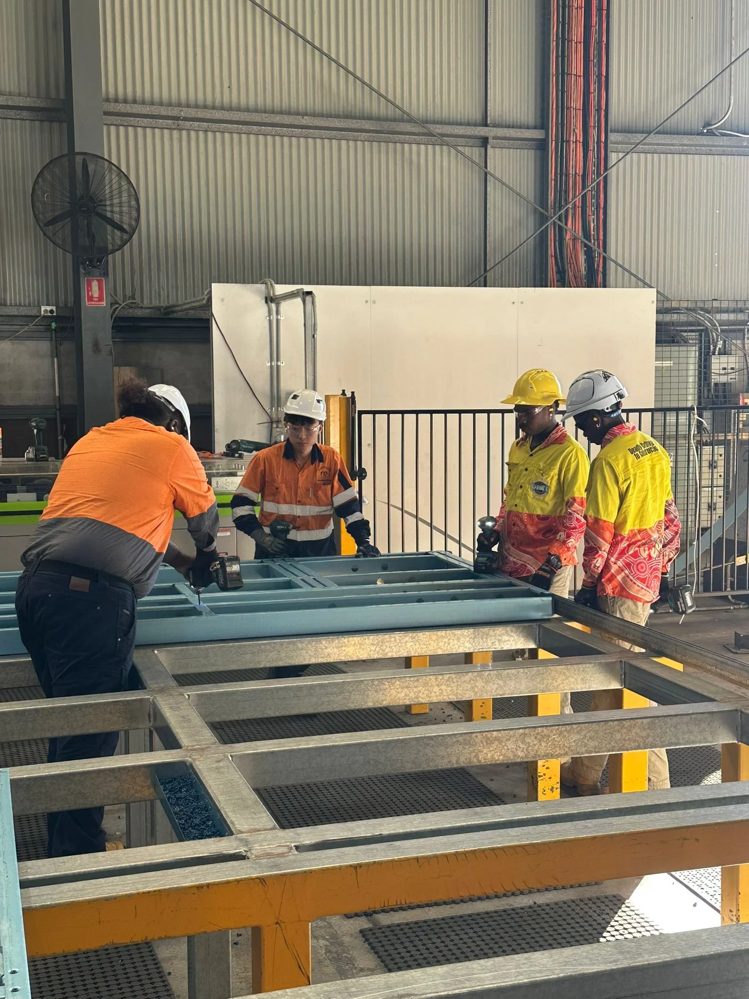 Workers in safety gear inspecting metal framework in an industrial setting.
