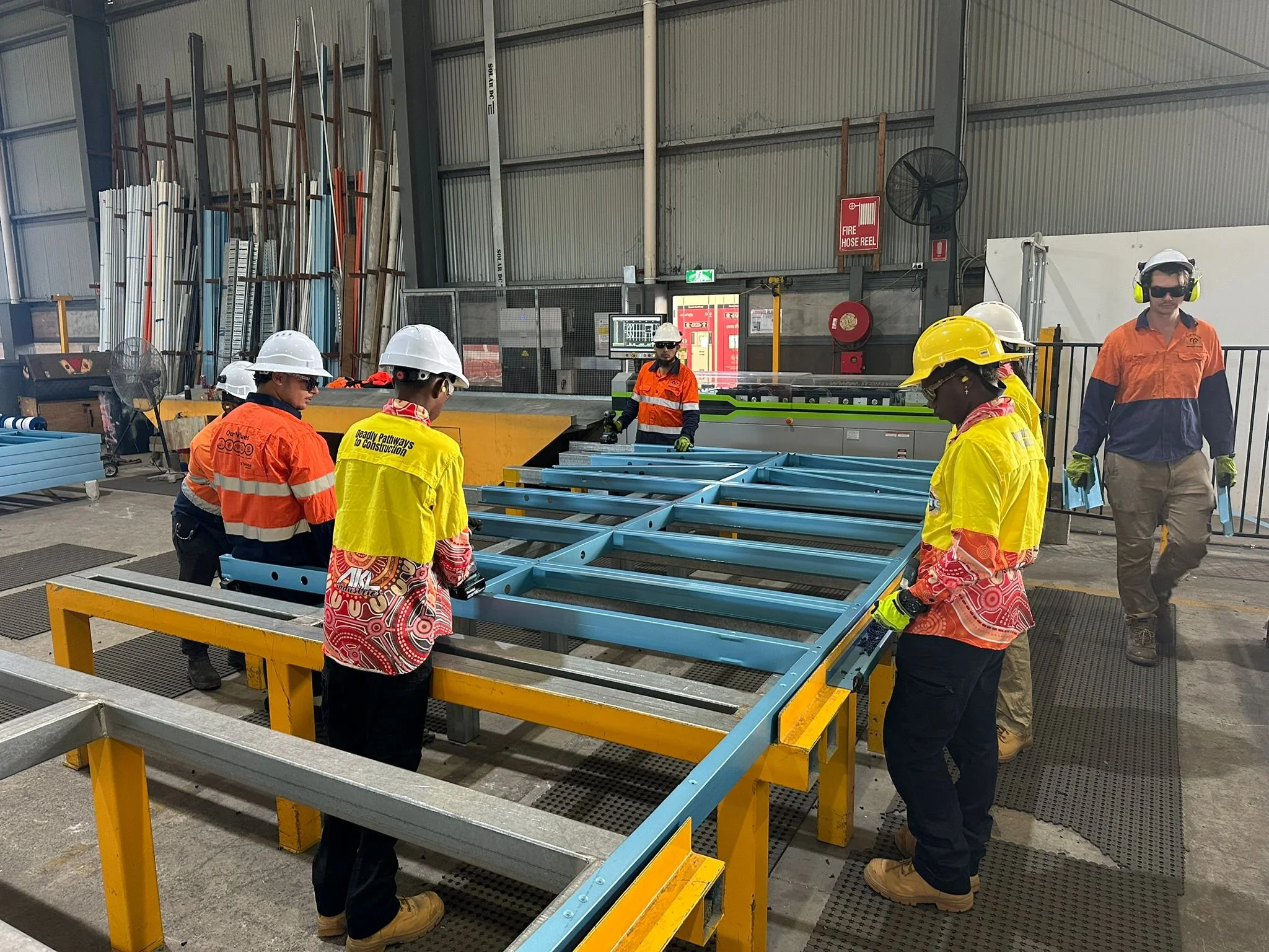 Workers in safety gear assembling a metal framework in an industrial warehouse.