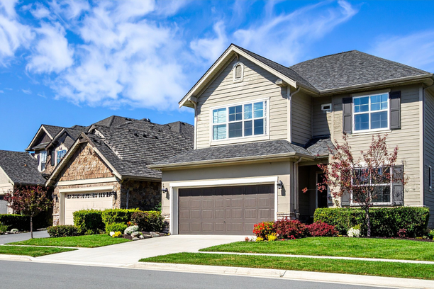 Two-story suburban house with a garage and manicured lawn under a partly cloudy sky.