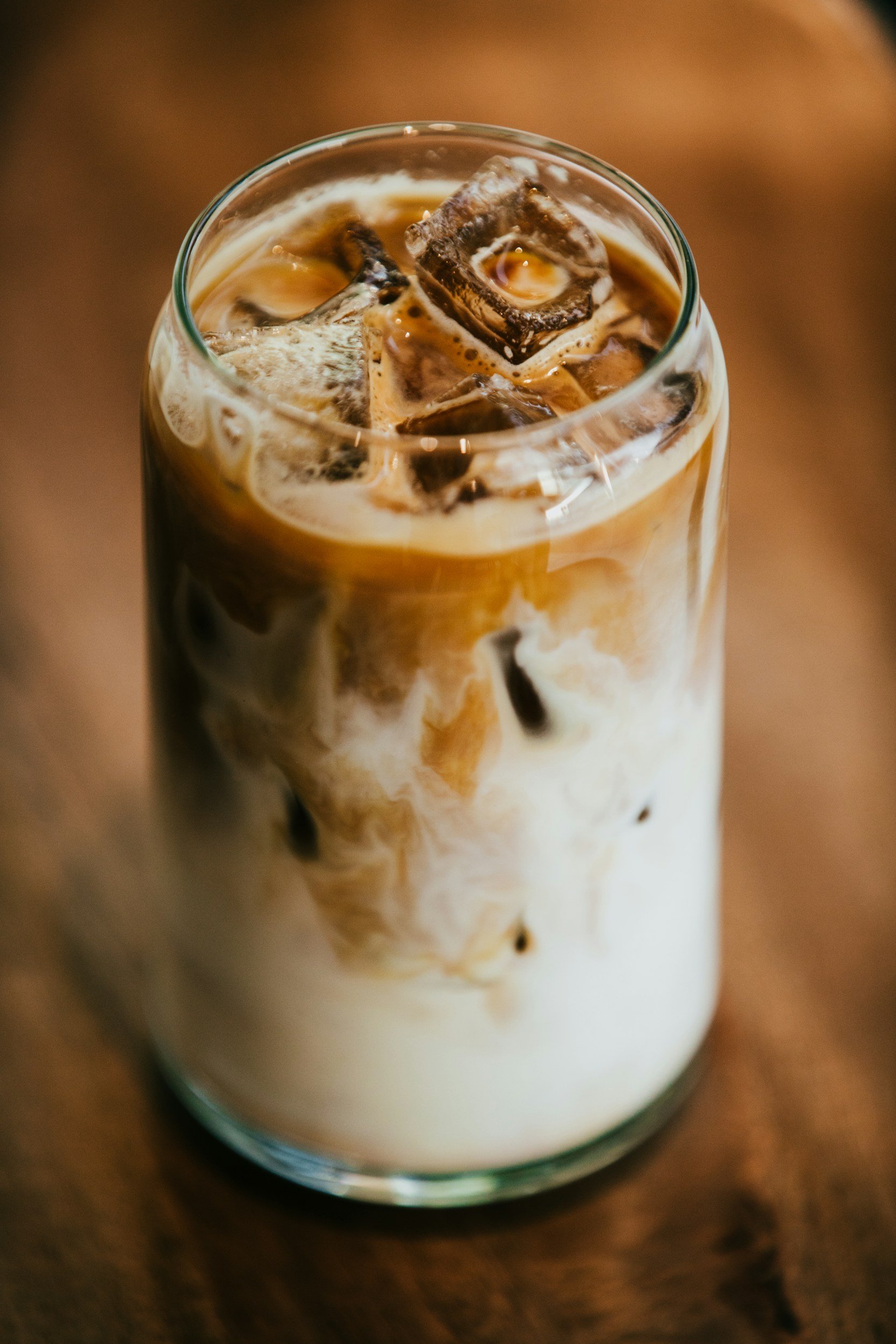 Close-up of a glass of iced coffee with swirling cream and ice cubes.