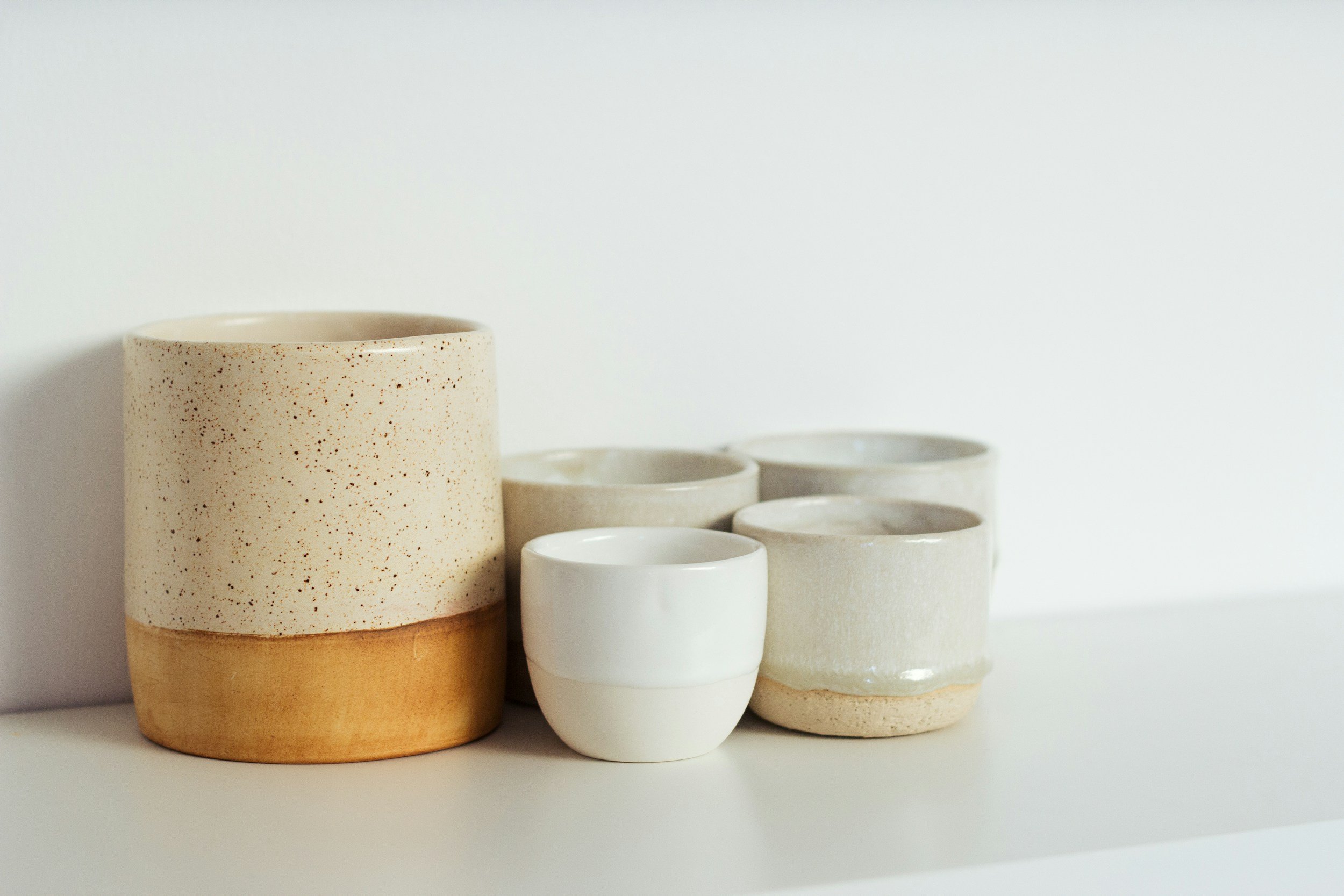 Set of minimalist ceramic cups and containers in neutral tones, arranged on a white surface against a plain white background.