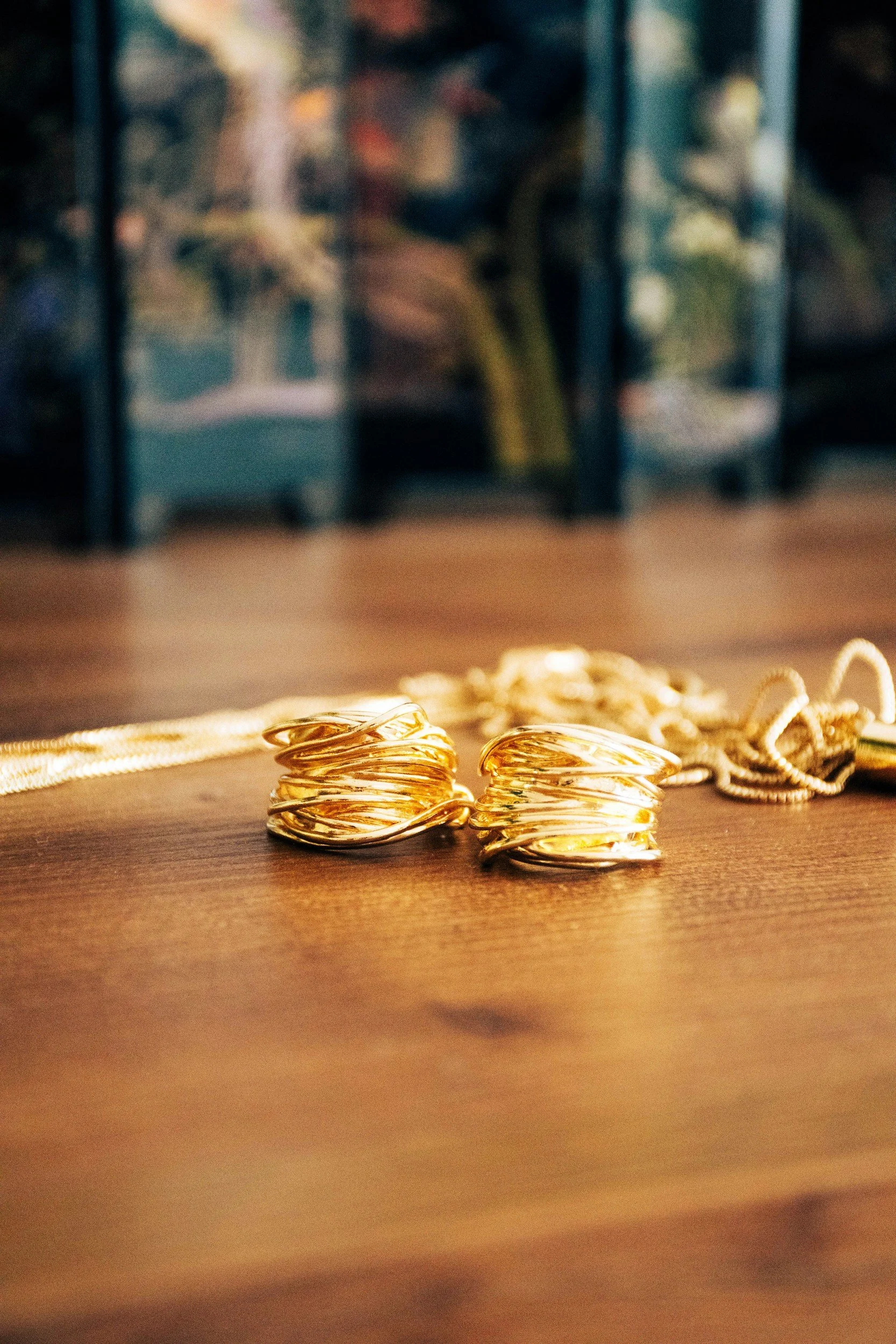 Gold jewelry pieces, including a necklace and earrings, resting on a wooden surface with glass doors and trees visible in the background.