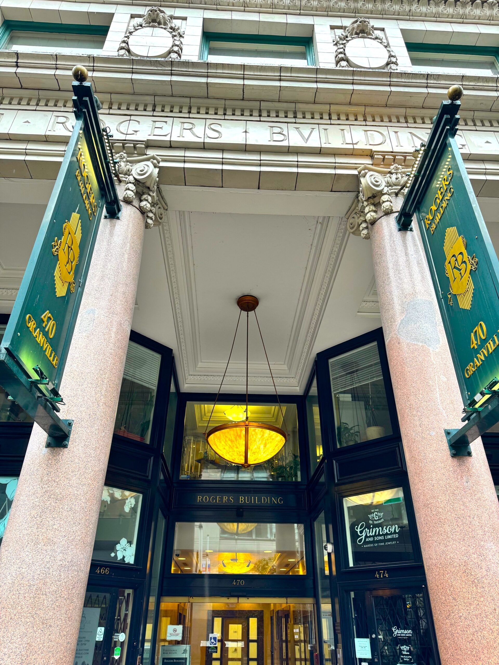The entrance of the Rogers Building with large pink columns, green and gold banners, and a glass door.