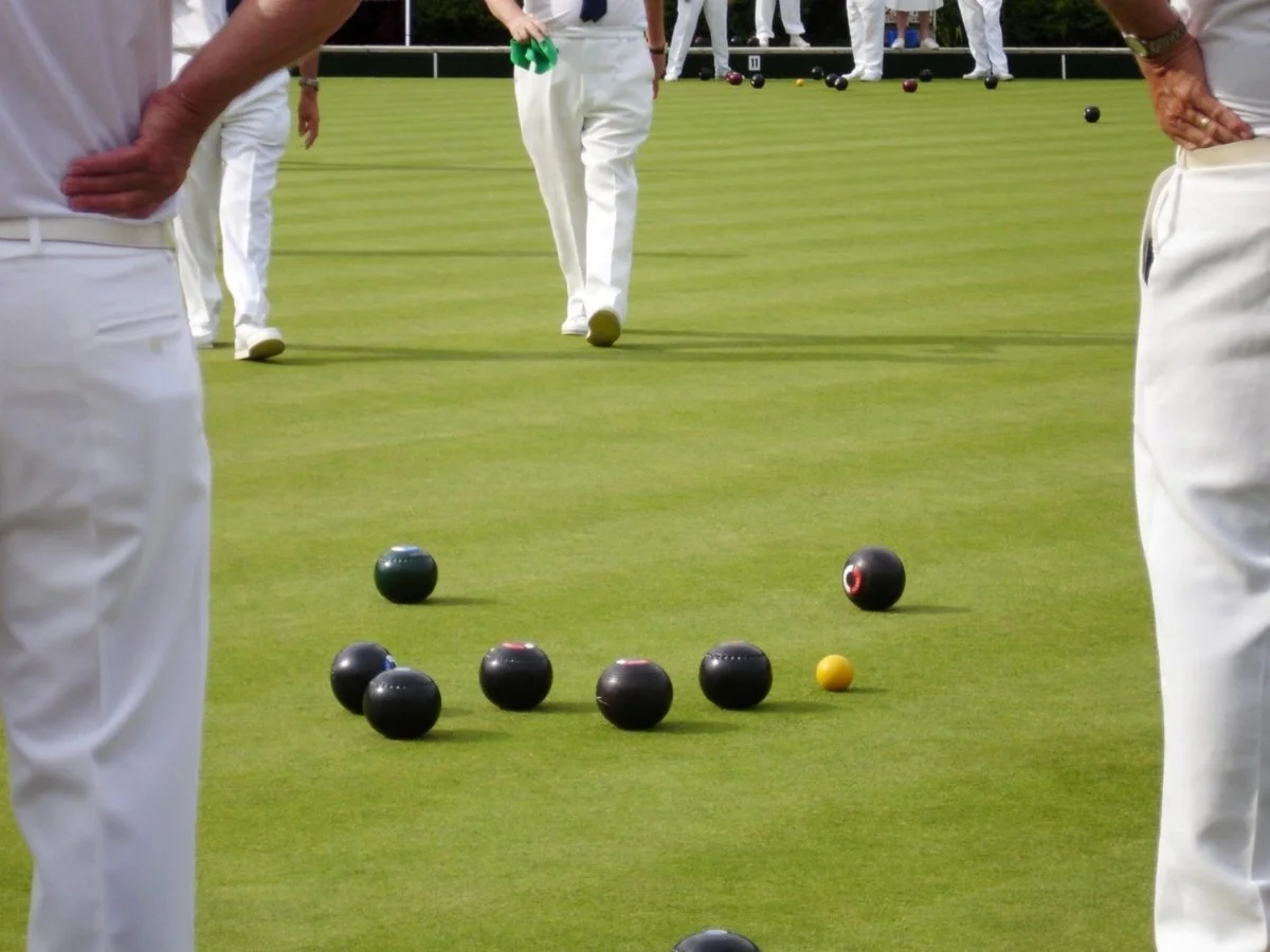 People playing lawn bowls on a green, with several black, one yellow, and some additional bowls nearby.