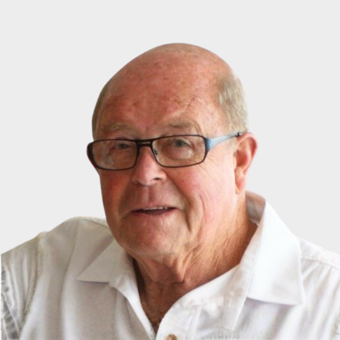 An elderly man wearing glasses and a white collared shirt, smiling.