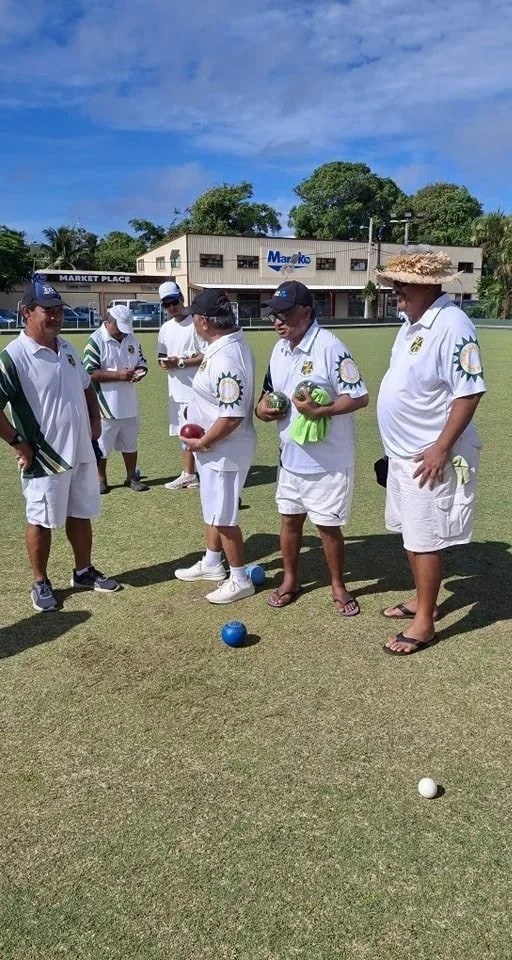 A group of men playing lawn bowls on a field under a partly cloudy sky, some holding bowls and others observing.