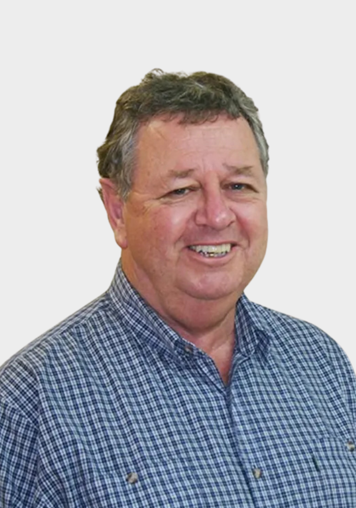 A middle-aged man with short, curly brown hair smiling, wearing a blue checkered shirt, against a plain white background.