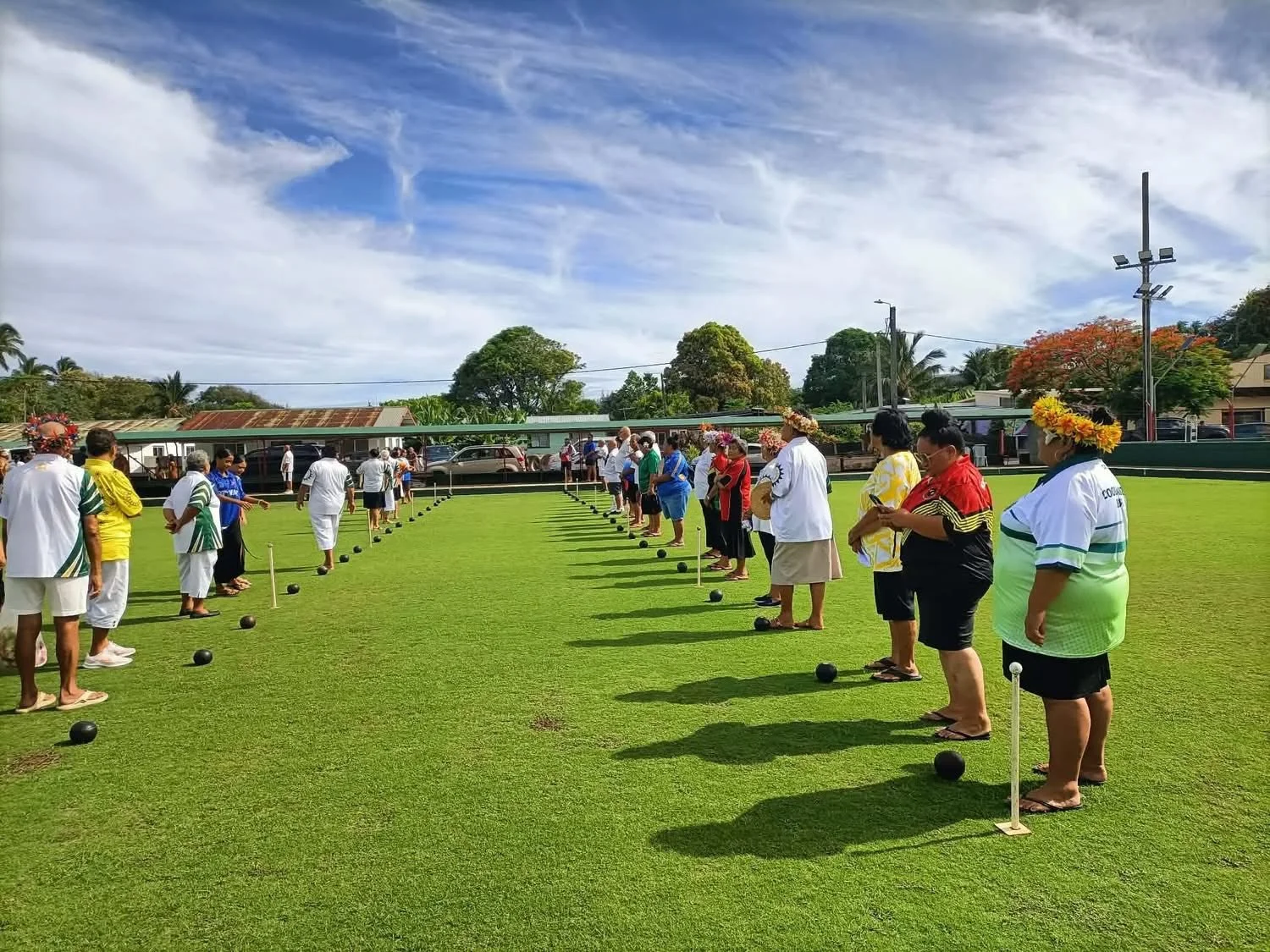 People participating in an outdoor game of lawn bowls on a green field on a sunny day.