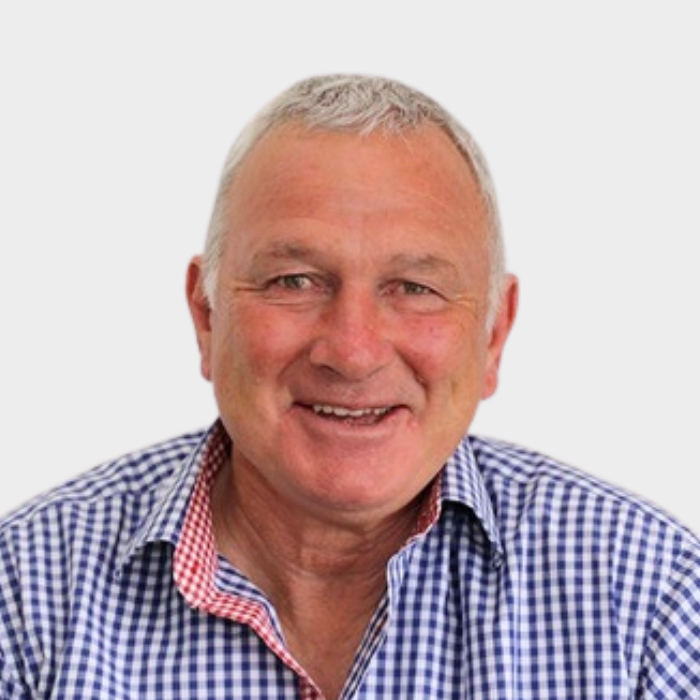 Portrait of an older man with short gray hair, smiling, wearing a blue checkered shirt, against a plain light background.