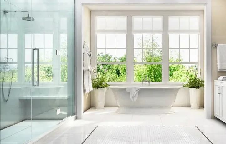 Bright bathroom with large window, freestanding bathtub, white towels, and potted plants.