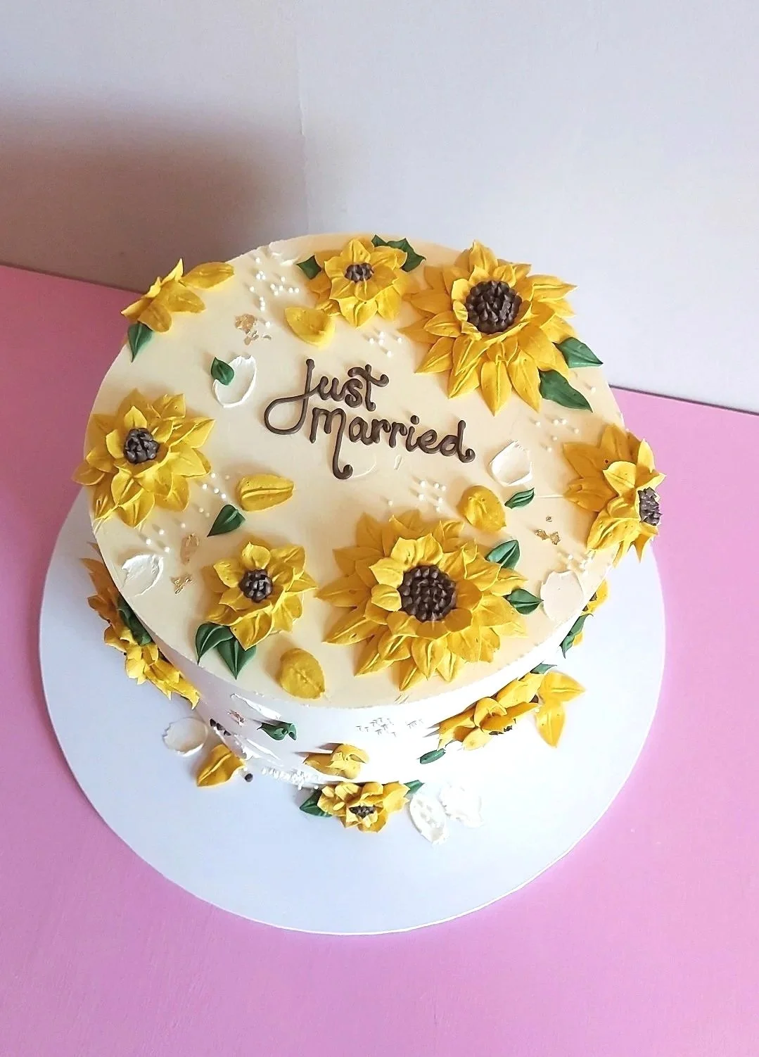 Wedding cake decorated with yellow sunflowers, white and gold accents, and the message 'Just Married.'