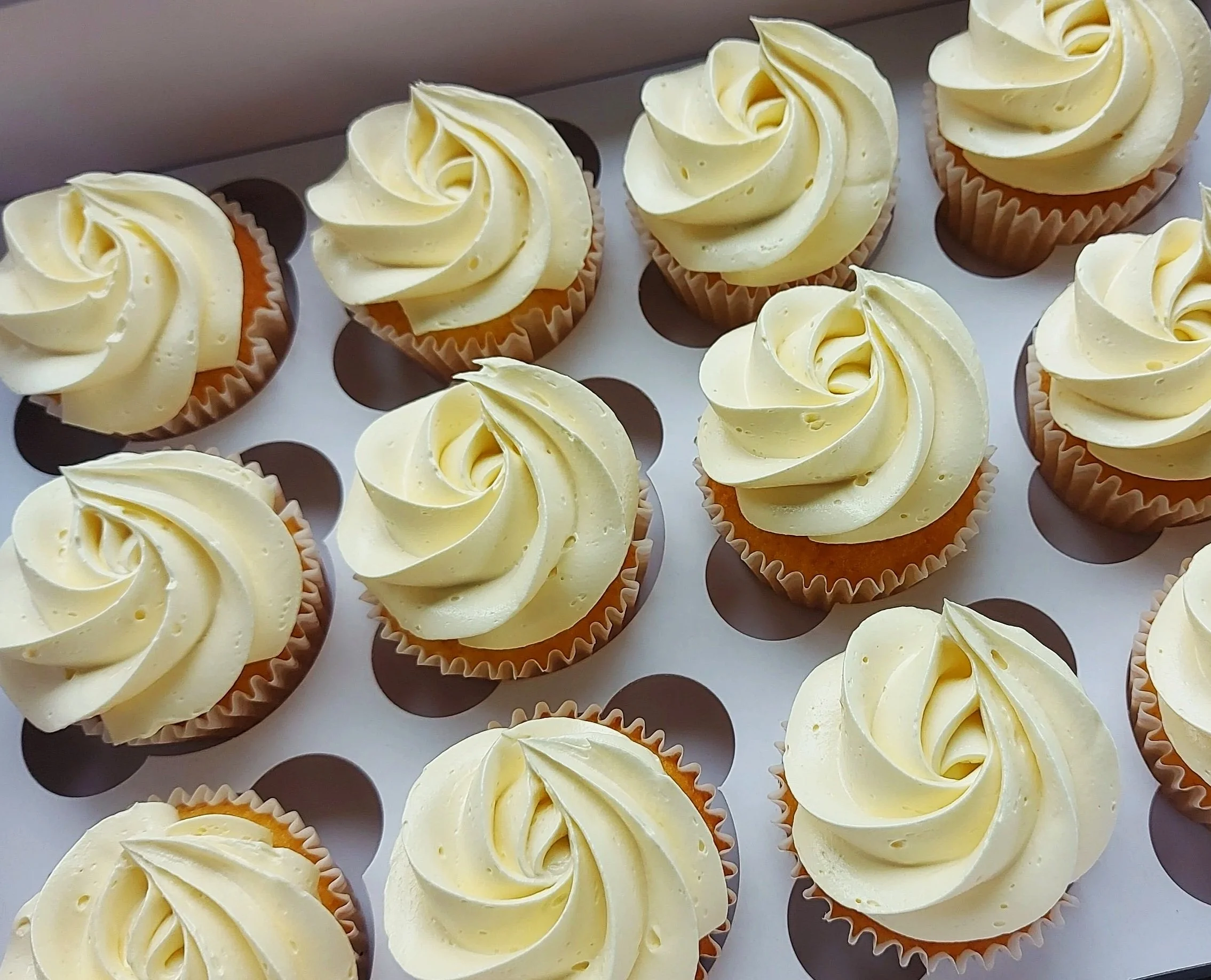 Several vanilla cupcakes with swirl frosting on top arranged on a white tray.