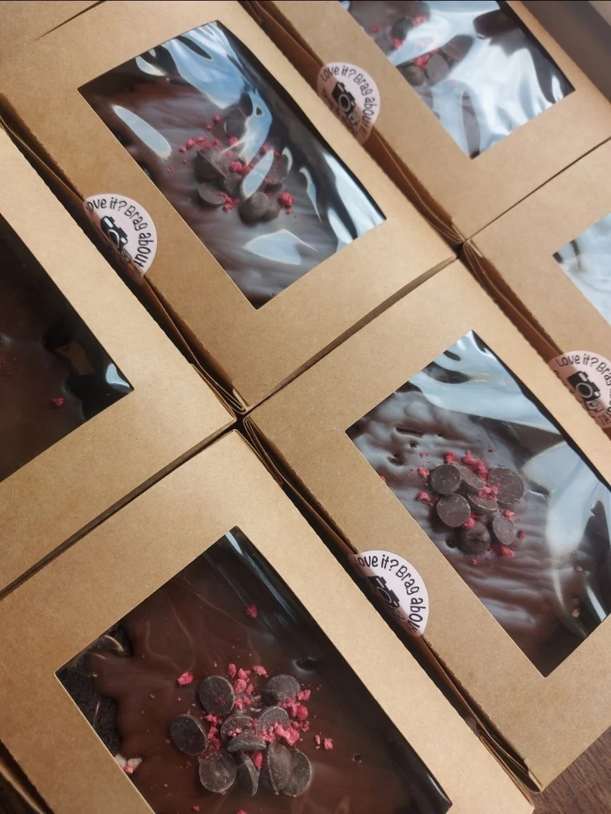 Chocolate cakes with chocolate chips and pink sprinkles inside cardboard boxes with window openings.