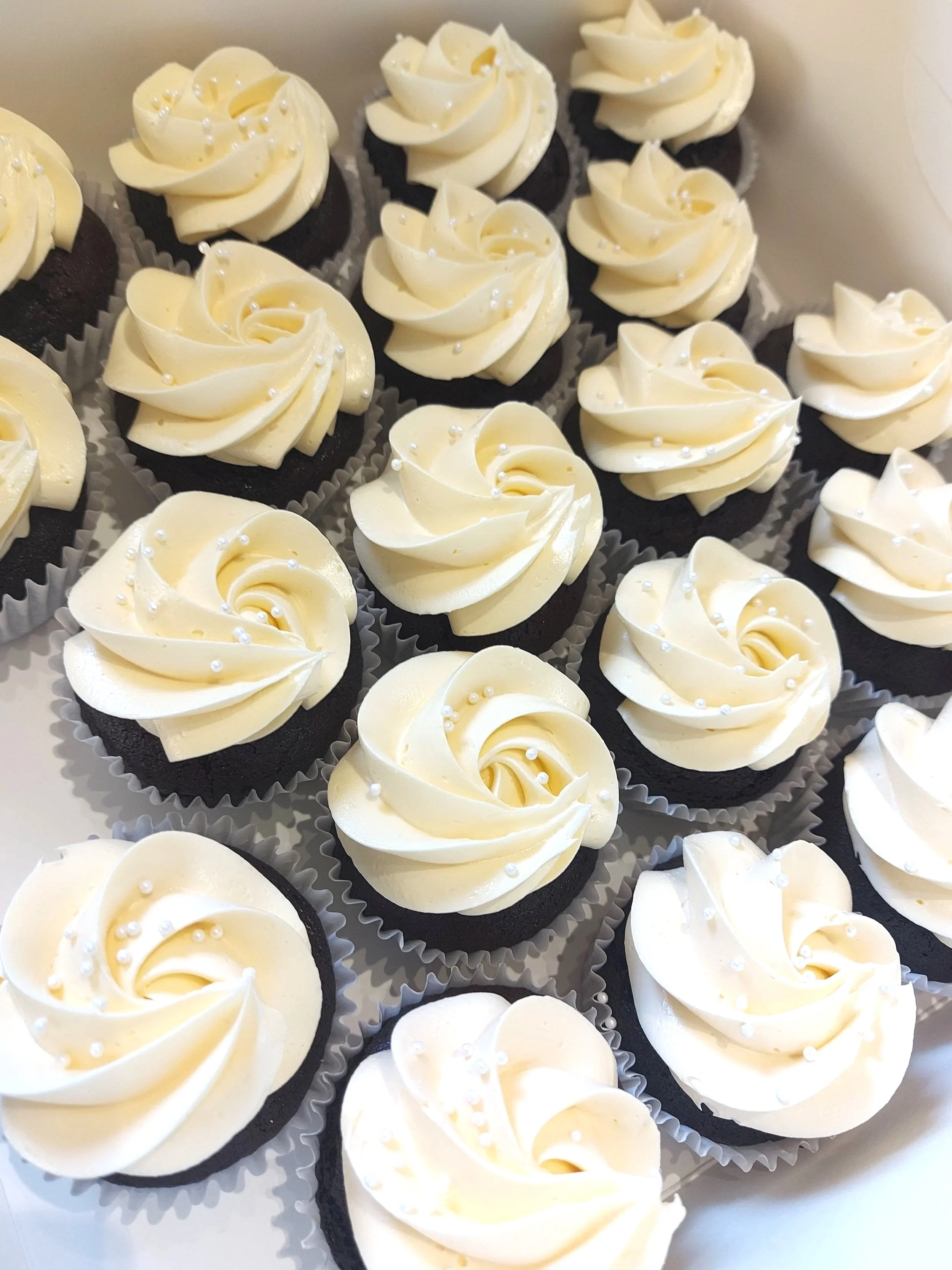 Chocolate cupcakes topped with white frosting and small white decorative pearls.