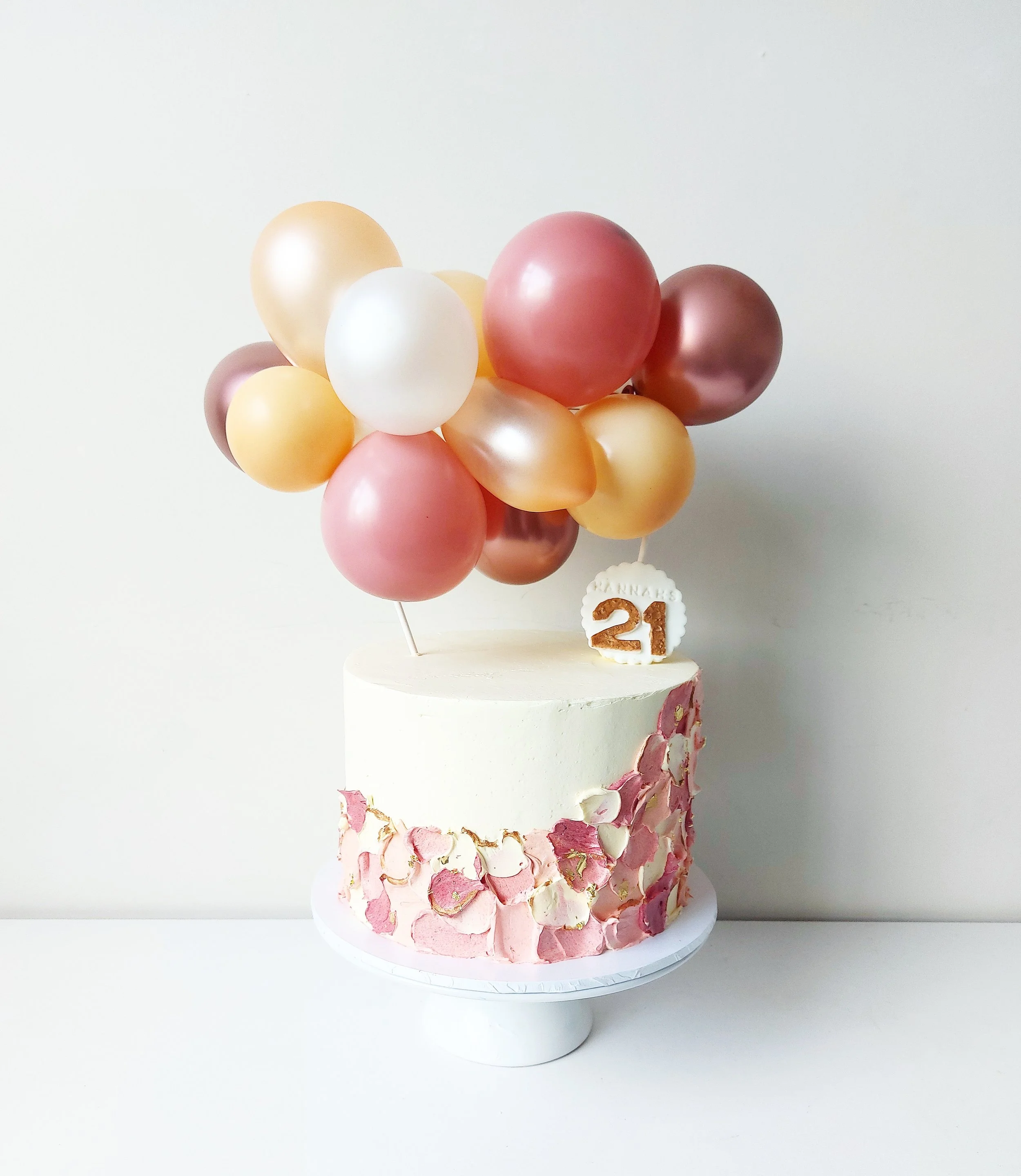 Balloons in shades of pink, peach, white, and metallic gold arranged in a bouquet on top of a pink and white marbled cake with a '21' cake topper, celebrating a 21st birthday.