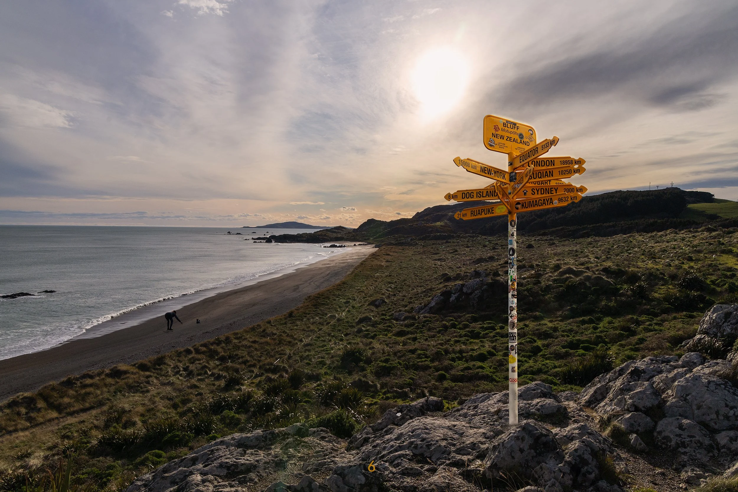 An image of a sign post sitting on a hill peak with a sunset and ocean surrounding.