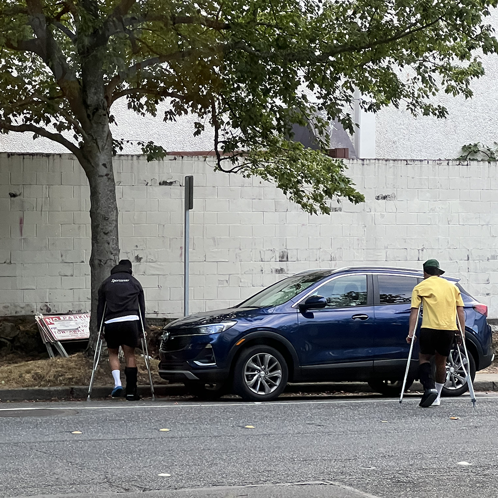 Two young male athletes crossing the street to their car following physical therapy rehabilitation session for their surgical procedures.
