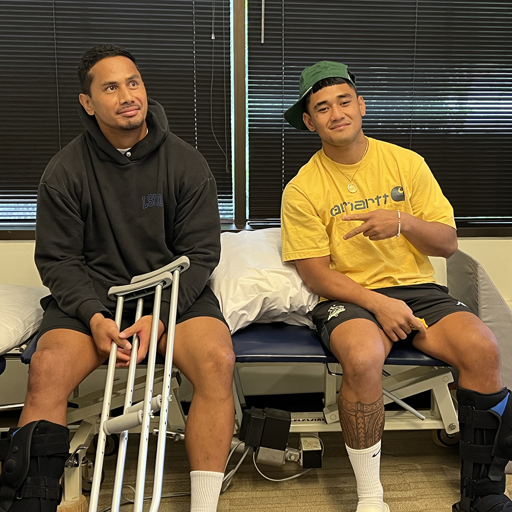 Two young male athletes sitting on a treatment table. They are about to begin physical therapy rehabilitation sessions for their surgical procedures.