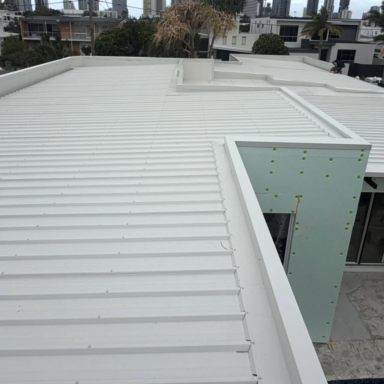 View of a white metal roof on a modern building, with green construction insulation and cityscape in the background.