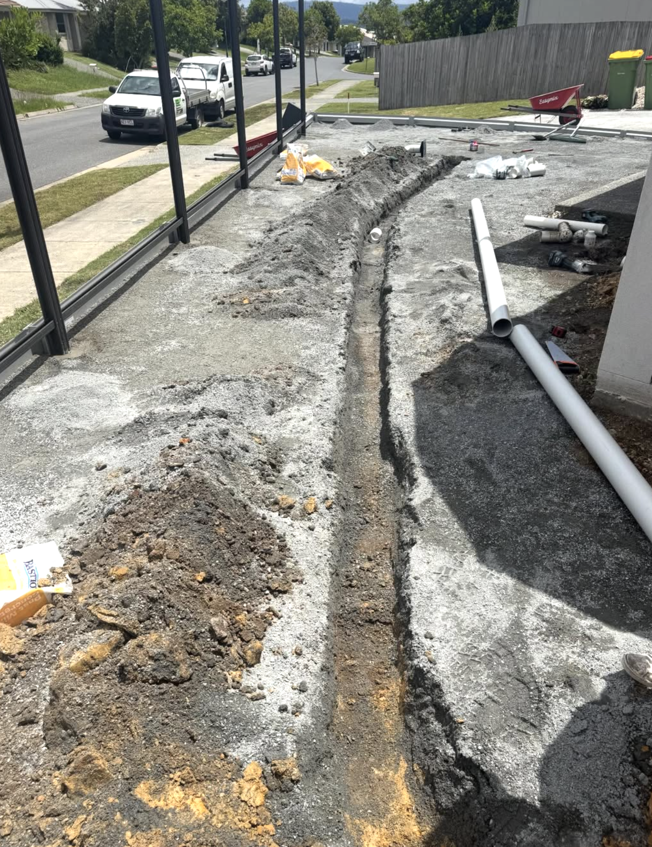 Construction site on a sidewalk with pipes and gravel, preparing for trenching or plumbing work.