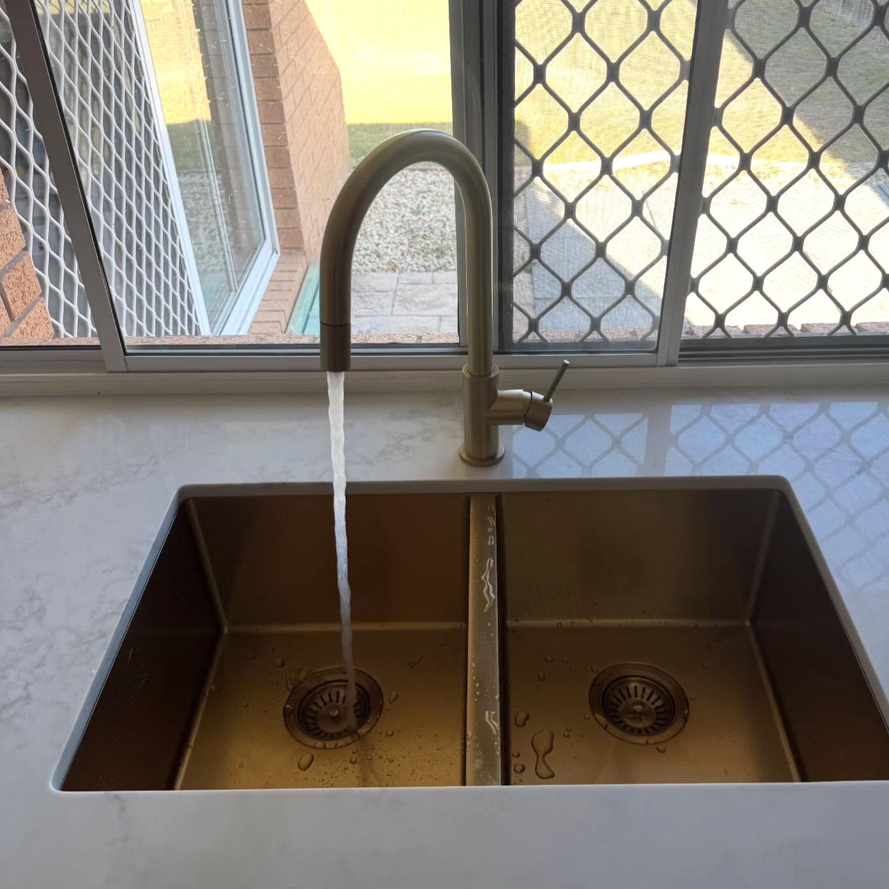Kitchen sink with running water and a view outside through a window with safety screens.