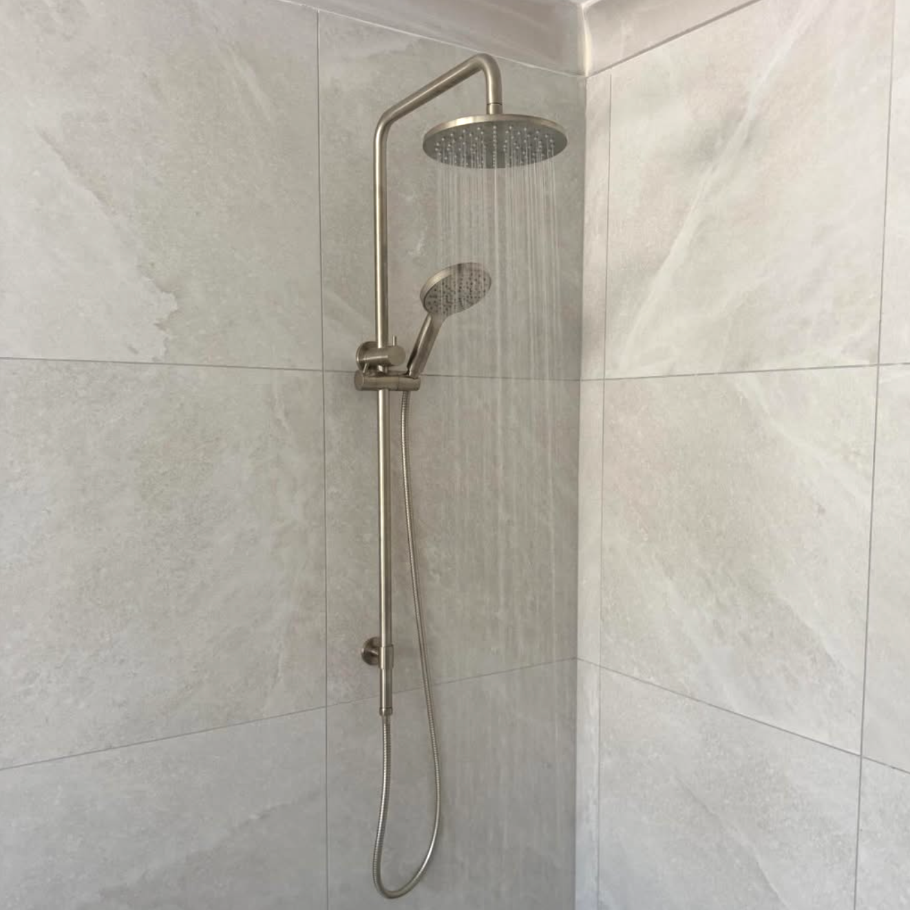Showerhead with a handheld attachment on a tiled bathroom wall