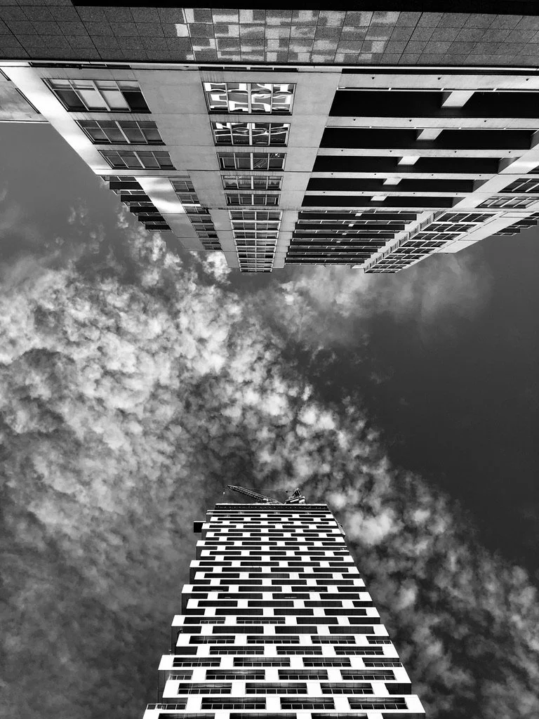 Black and white photo of tall modern buildings in Vancouver, BC, Canada from ground level looking up, with clouds in the sky.