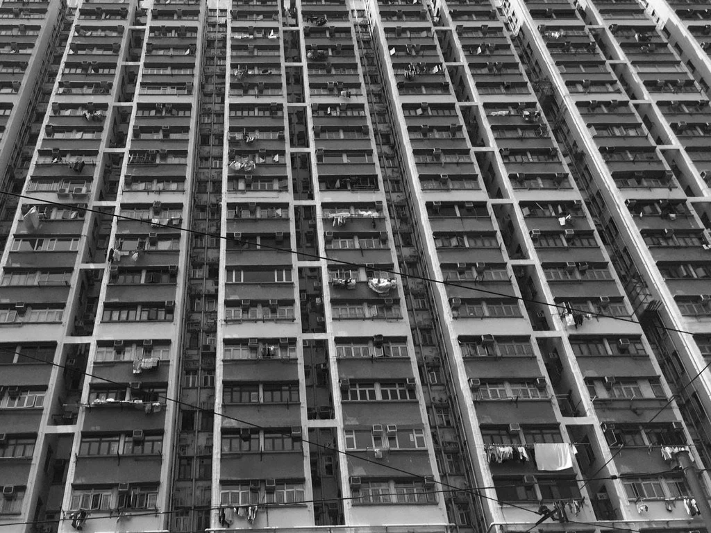 A black and white photo of a tall apartment building with many windows and balconies, some with laundry hanging outside.