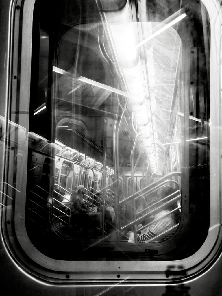 Inside a subway train with passengers sitting and standing, view through a window, black and white photo.