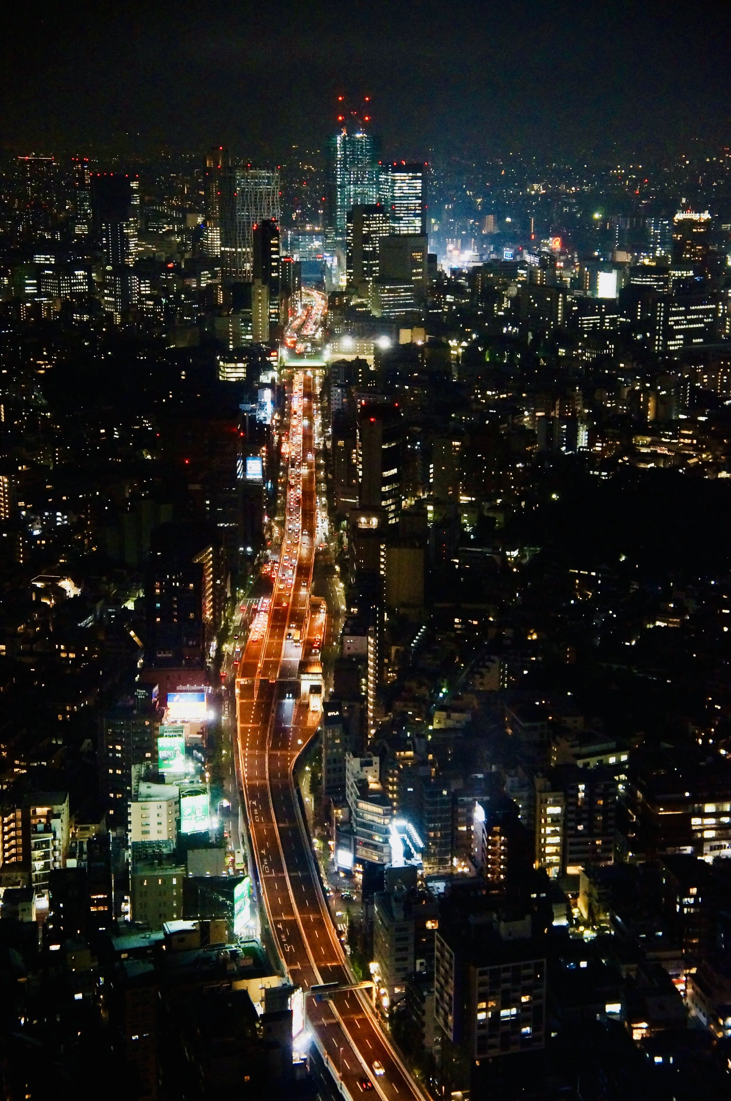 Nighttime cityscape featuring illuminated skyscrapers, streets with moving traffic, and numerous buildings with lit windows.