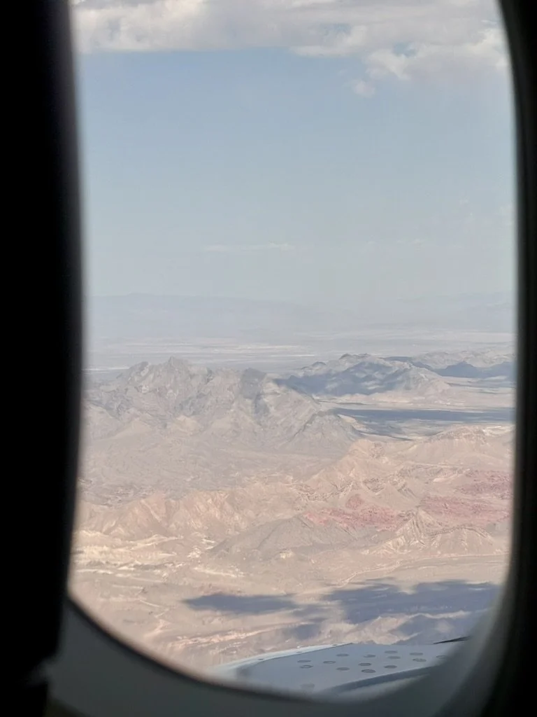 Aerial view of a desert landscape with mountains seen through an airplane window.