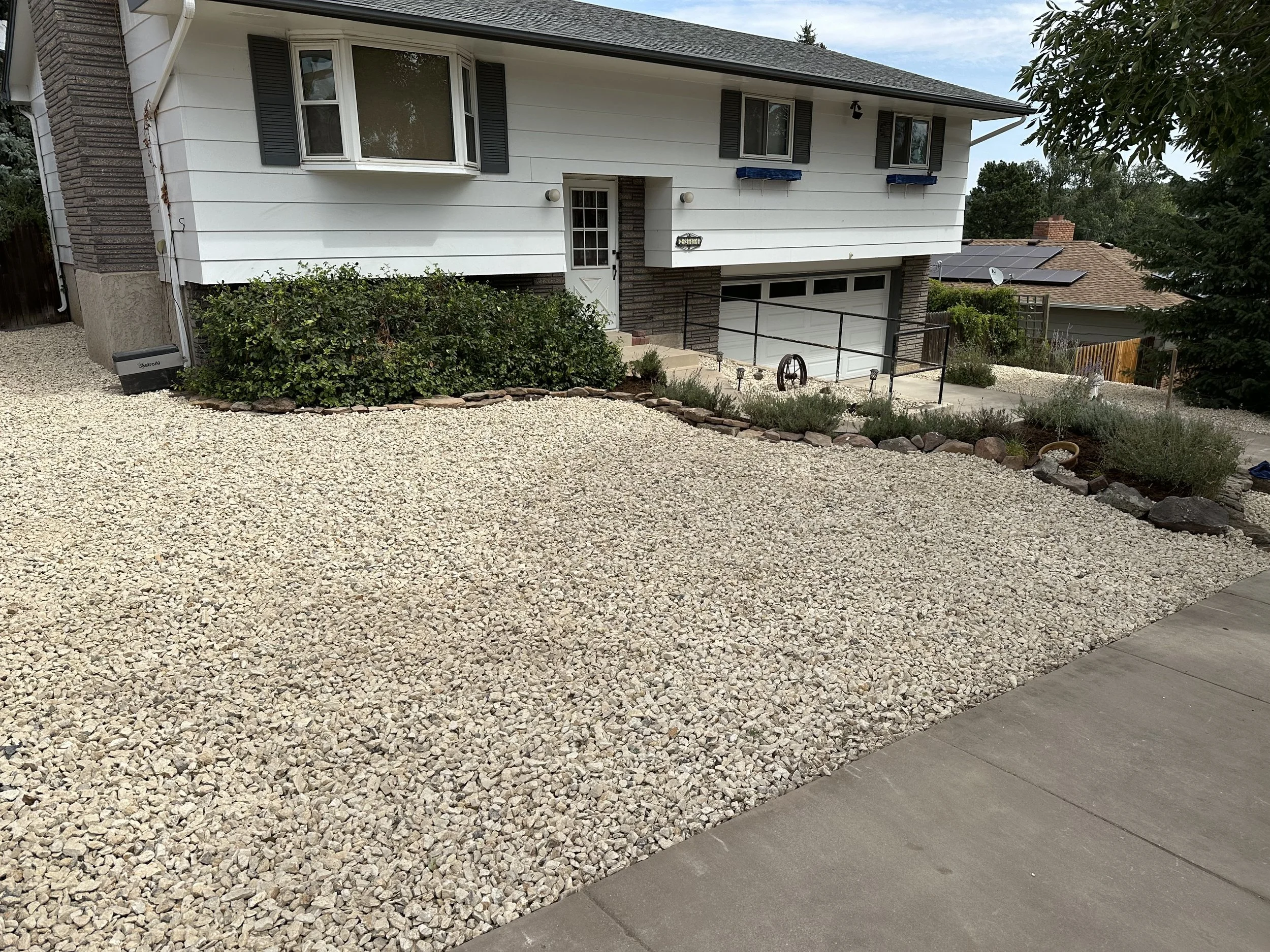 Front yard of a house with gravel landscaping, a bush near the front door, and a driveway with a garage.