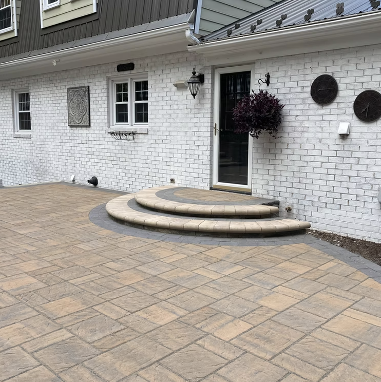 A white brick house with a small black lantern above and a door with a black handle. There are three curved steps leading to the door, surrounded by a paved patio. The house has a window with two smaller windows on the side, and decorative black wall