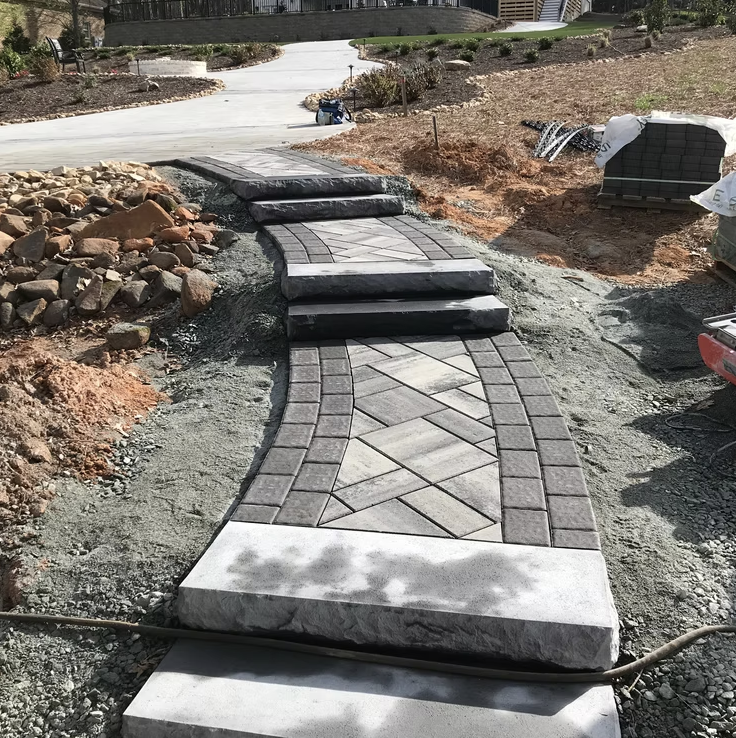 Under construction pathway with steps and decorative paving stones in a landscaped yard.