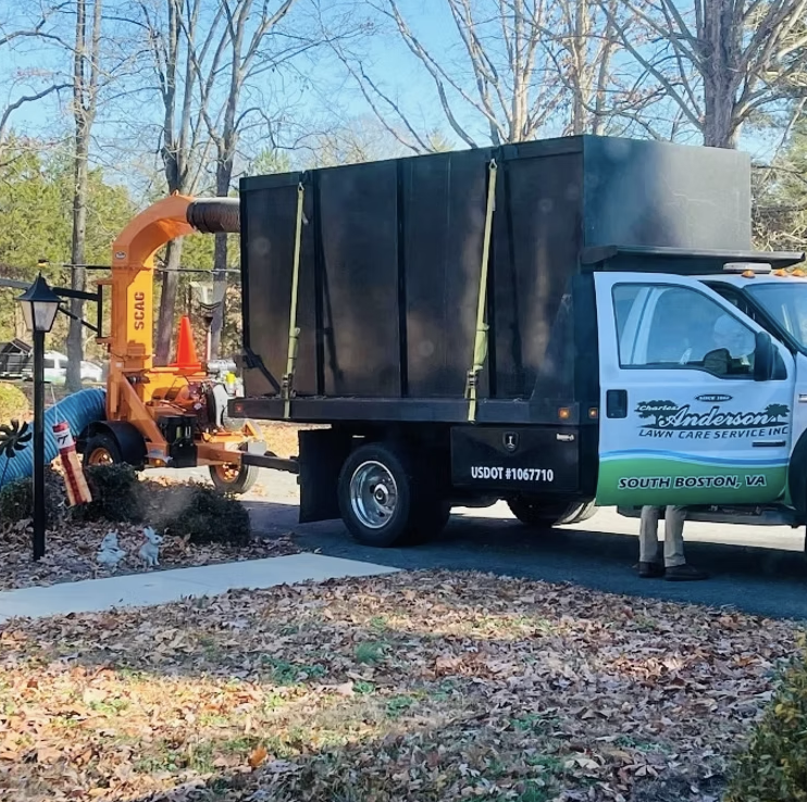 Lawn care service truck from Anderson Lawn Care Service Inc. with equipment, parked on a suburban street with trees and autumn leaf-covered yard.