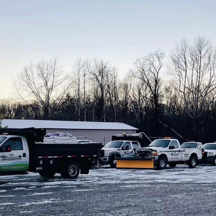 A row of service trucks parked on a snowy ground, with trees and a building in the background.