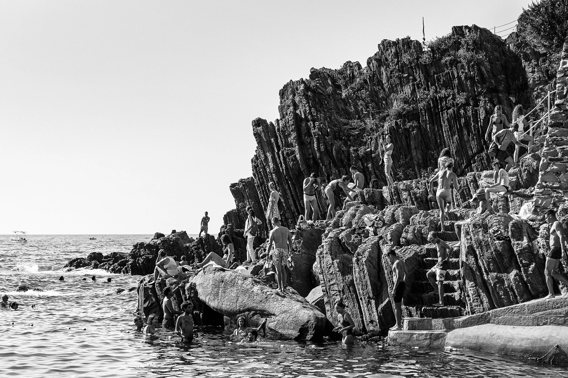 People swimming, climbing, and relaxing on rocks by the ocean on a sunny day.
