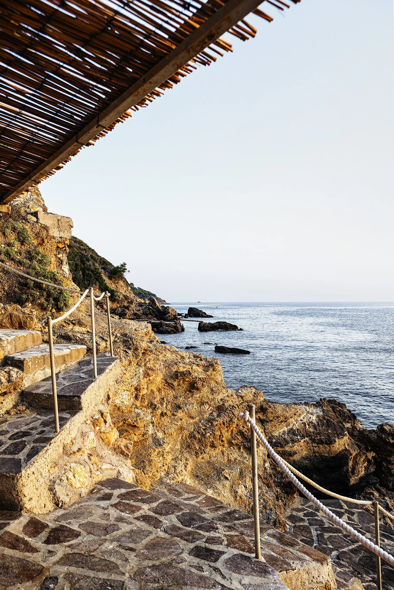 Stone staircase along rocky coastline with railing, overlooking the ocean at sunset.