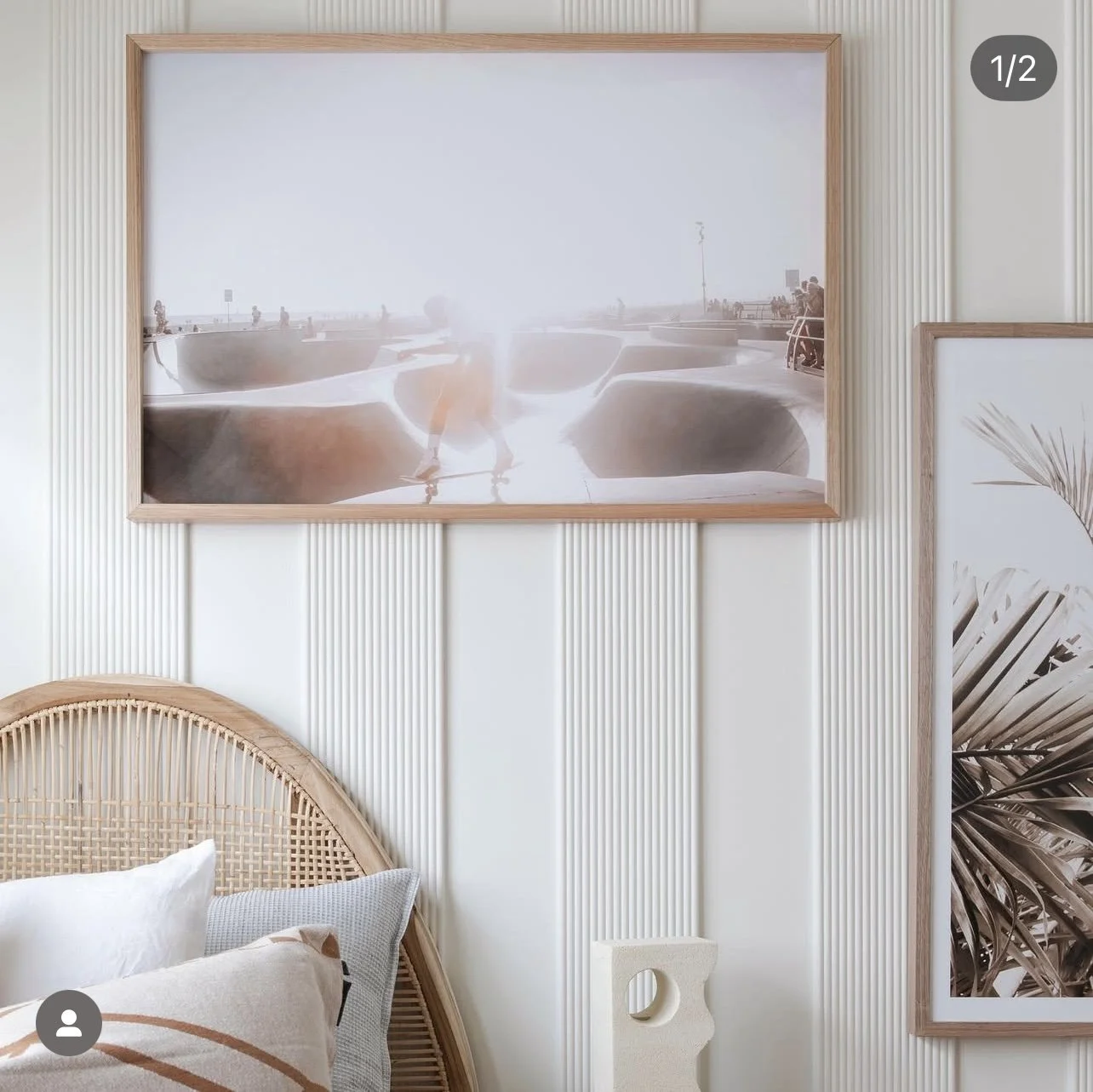 A bedroom with a bed and pillows, a framed photo on a textured wall, and a partial view of another framed picture with a palm leaf design.
