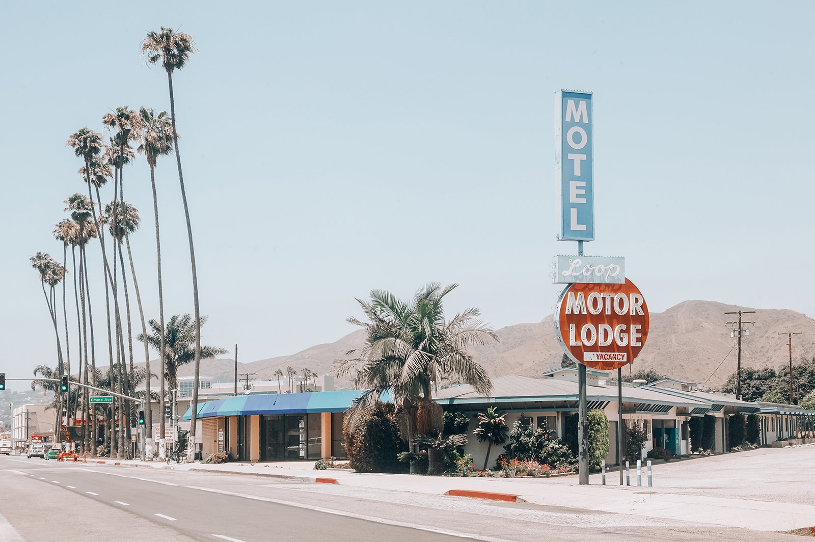 Vintage motel and motor lodge sign, surrounded by palm trees, with a mountain background and clear sky.