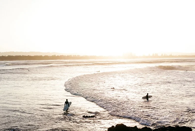People surfing on the ocean during sunset or sunrise.