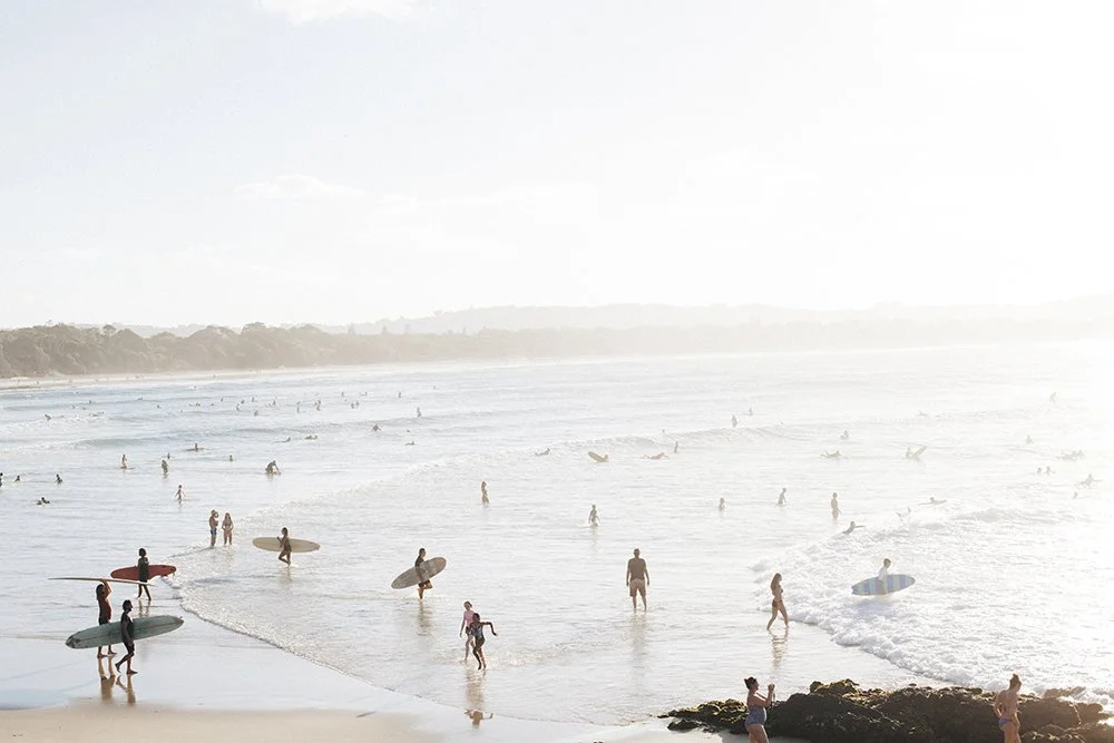 People surfing and wading in the ocean at a crowded beach during daylight.