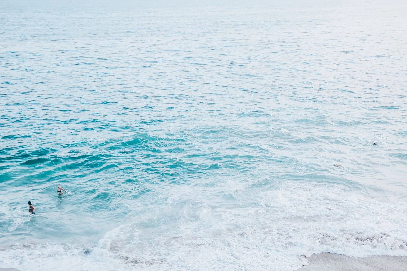 Three people swimming in the ocean near the sandy beach with gentle waves.