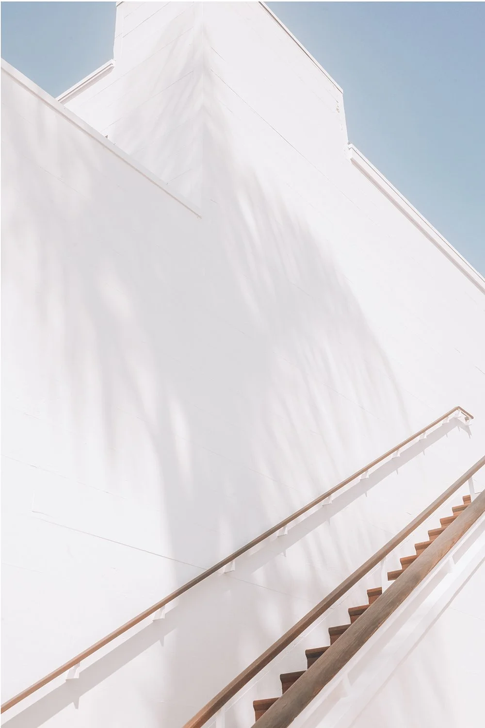 Minimalist white building with stairs and wooden handrails against a clear blue sky.